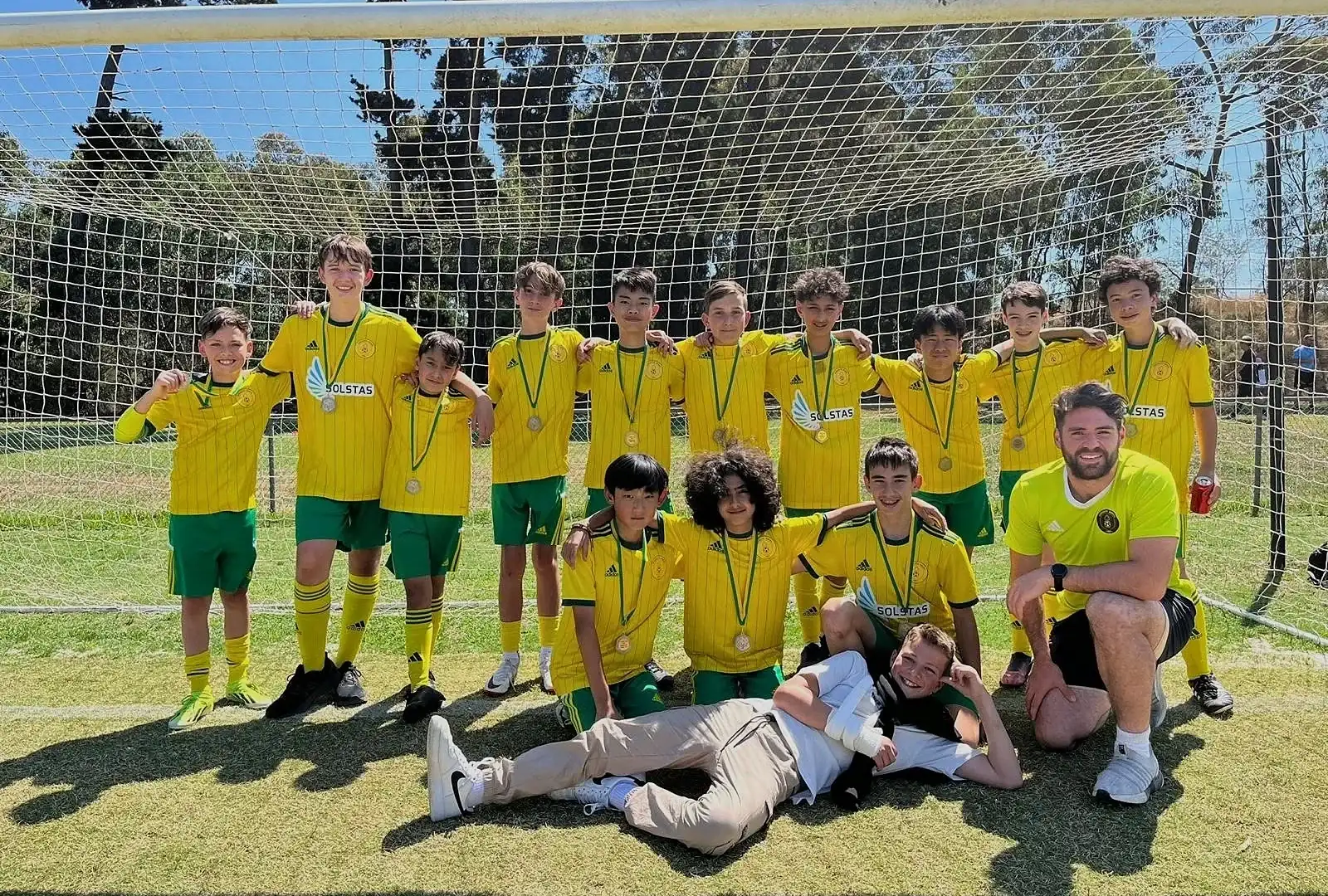 A Doncaster Rovers junior team and their coach in front of the goal, in the club’s yellow and green, wearing medals.